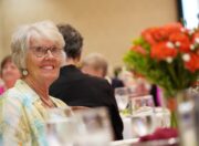Mary Lynne, left, smiling at her table across from a bouquet of persimmon-colored roses